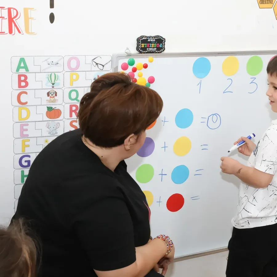 Educatoare lucrând la tablă cu un copil, la ora de numere